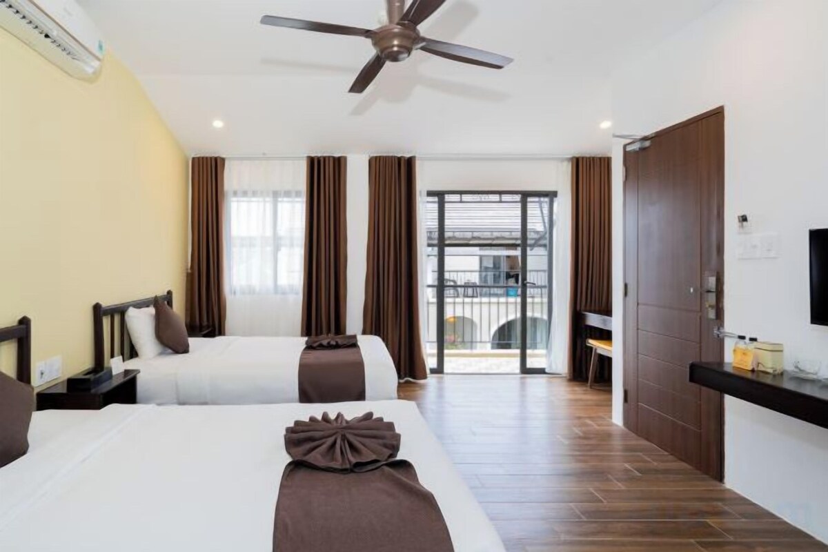 A hotel room with two beds, a ceiling fan, a TV, and a sliding door to a balcony.