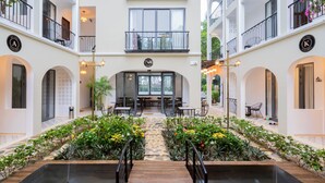 Um átrio de hotel com escadaria central, cercado por vegetação exuberante e um elemento aquático.