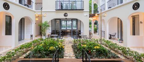 Un atrio de hotel con una escalera central, rodeado de abundante vegetación y una fuente de agua.