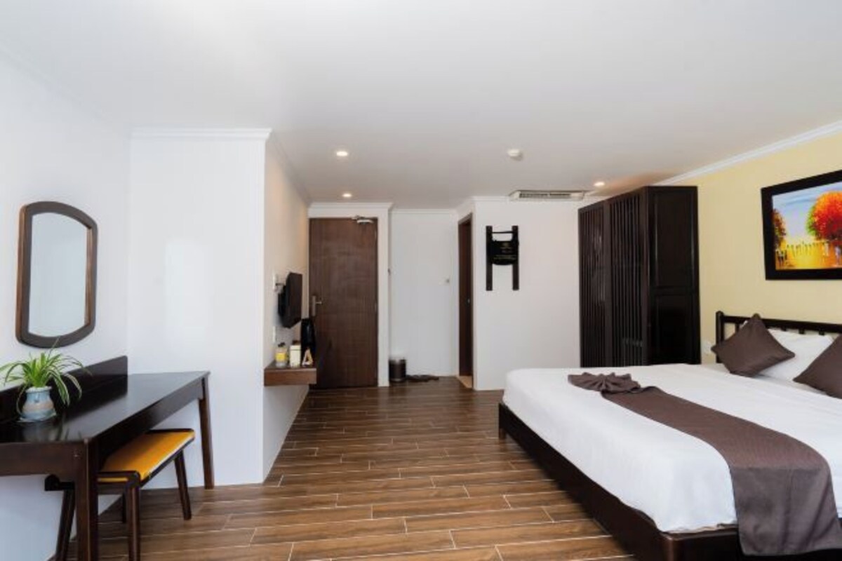 A hotel room with a bed, a desk with a chair, a mirror, and a painting on the wall.