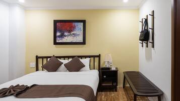 A hotel room with a bed, a nightstand, a lamp, a bench, and a wall-mounted coat rack.