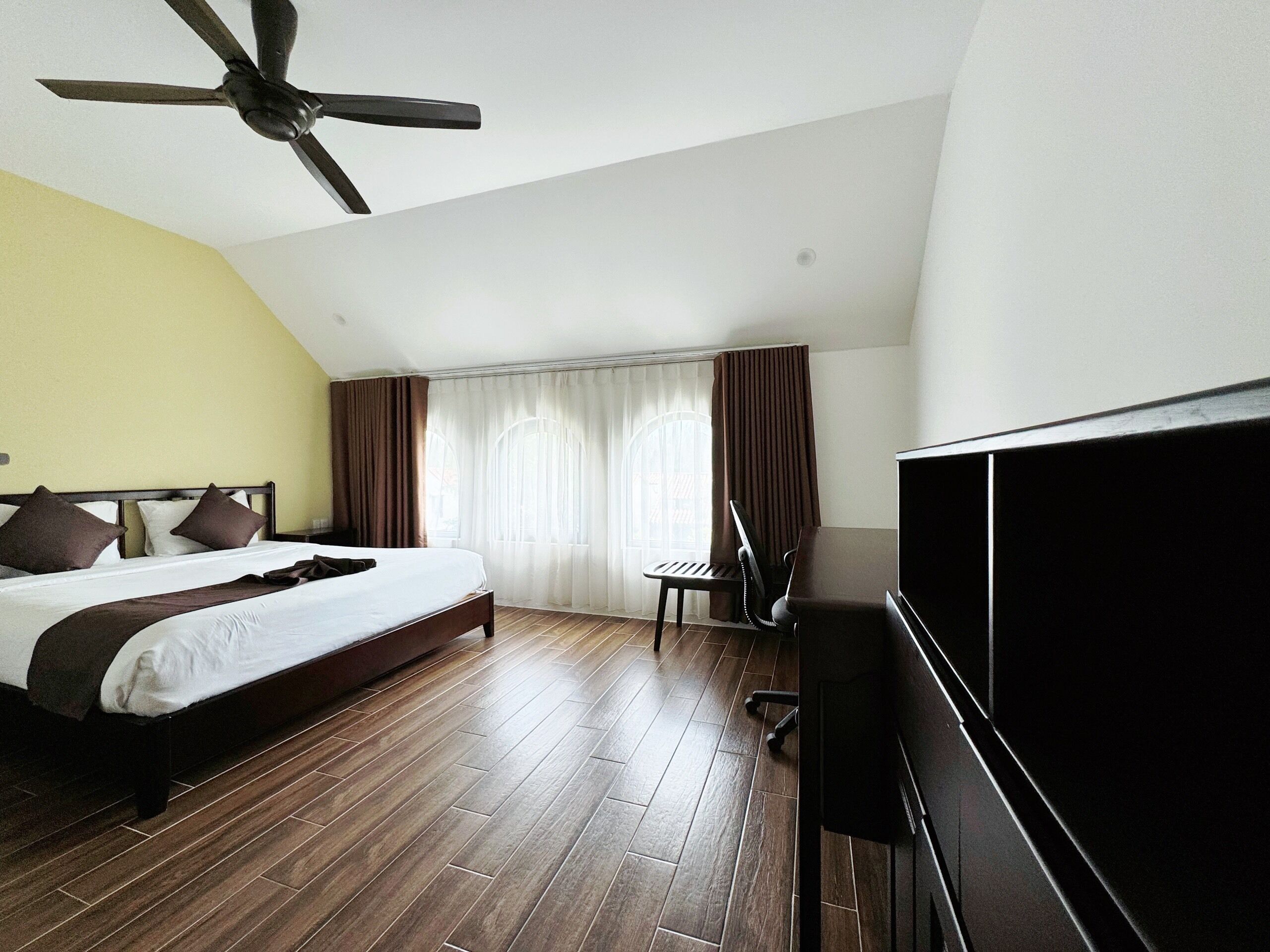 A hotel room with a bed, a desk, a chair, a television, and a ceiling fan.
