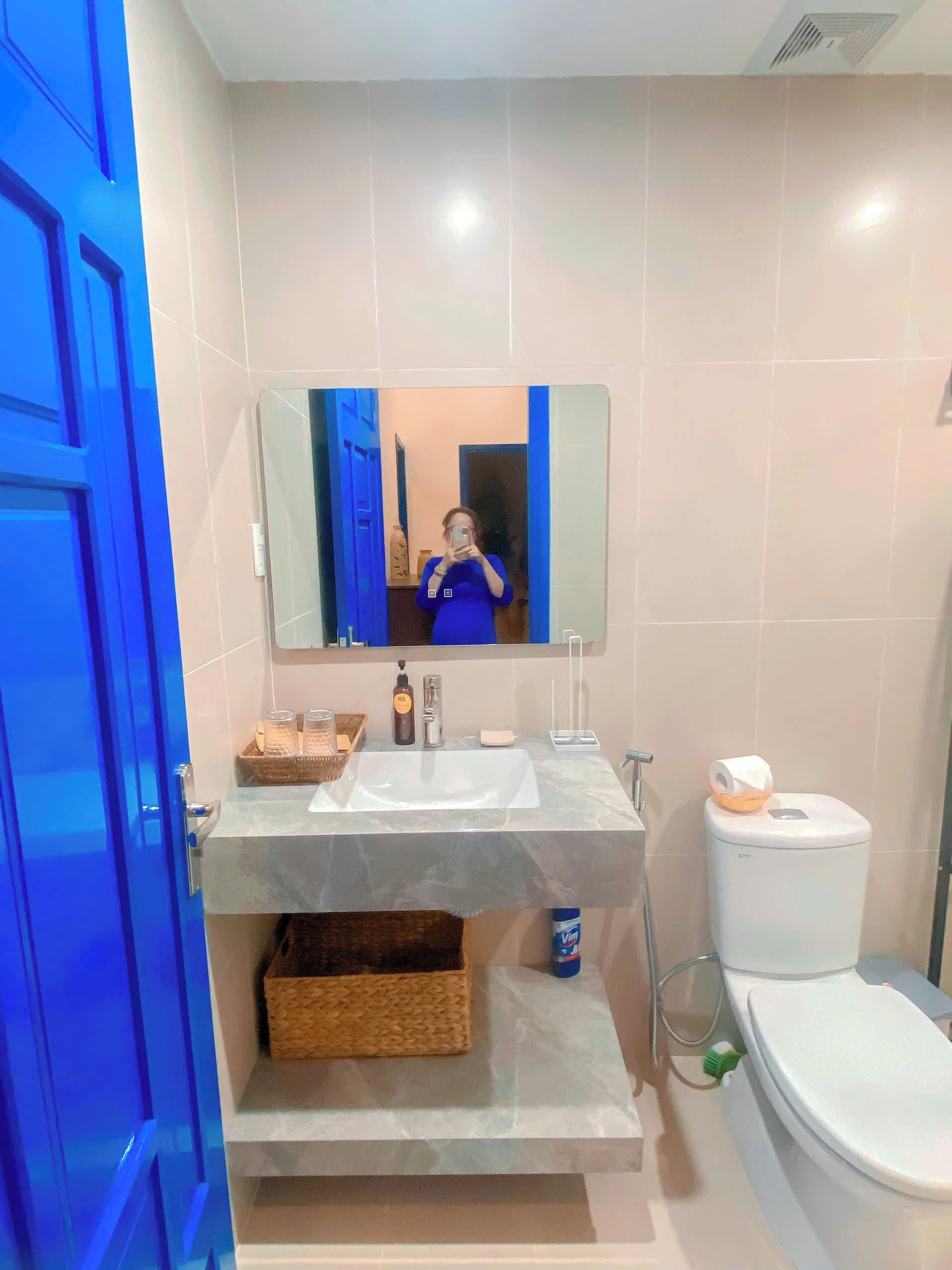 A bathroom with a mirror, sink, toilet, and a blue door.