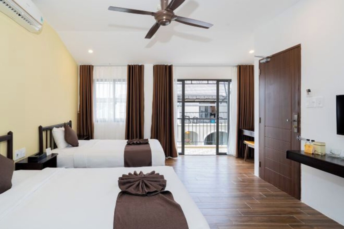 A hotel room with two beds, a ceiling fan, a TV, and a sliding door to the balcony.