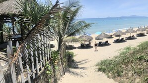 Uma praia com guarda-sóis de palha, cadeiras de descanso e vista clara do oceano.