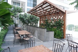 An outdoor patio with multiple tables and chairs, a wooden pergola, and lush greenery. - Studio Apartment near Airport (Ho Chi Minh City)