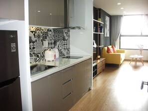 A modern kitchen with a built-in stove, a refrigerator, and a patterned backsplash. There is a yellow sofa and a small table with a vase of flowers in the living area. - Studio Apartment near Airport (Ho Chi Minh City)