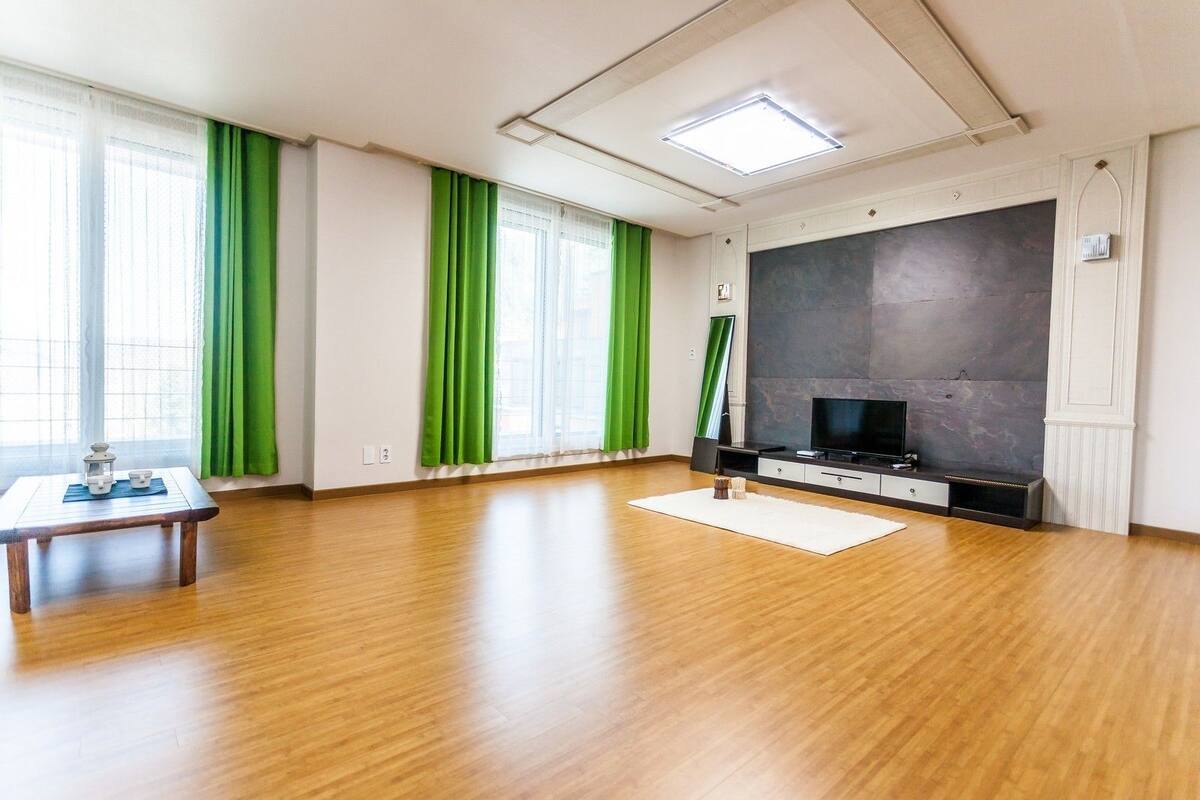A spacious living room with a wooden floor, a flat-screen TV, and a large dark wall.