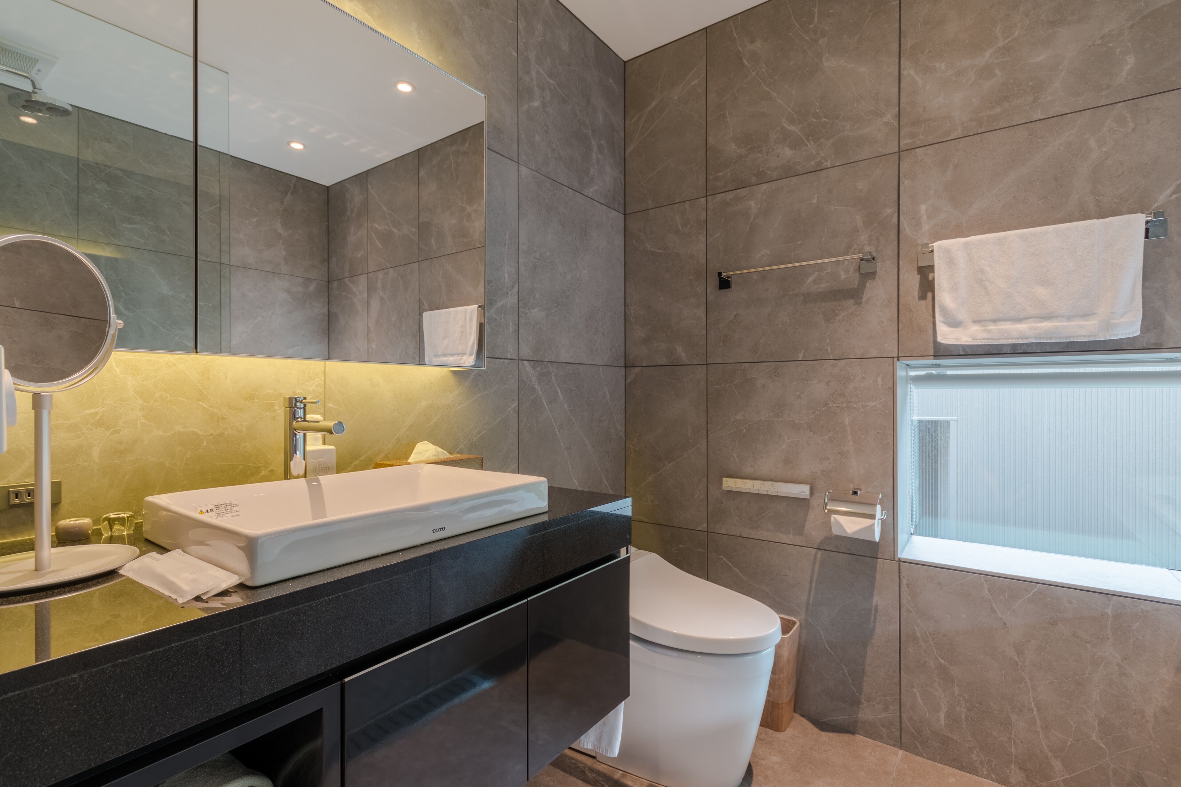 Une salle de bain moderne avec un grand miroir, un lavabo blanc et des toilettes.