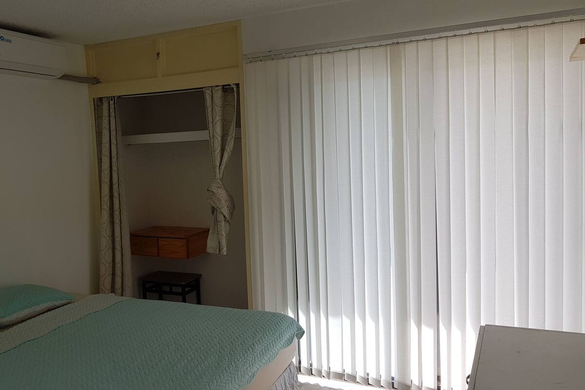 Ein Zimmer mit einem Bett, einem kleinen Tisch, einem Schrank und einem Fenster mit Jalousien.