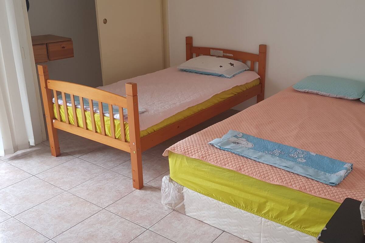 Ein Schlafzimmer mit zwei Einzelbetten, einem Holzsessel, einem kleinen Nachttisch und einer Aufbewahrungsbox.