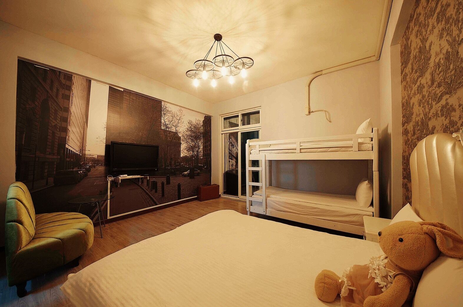 Habitació d'hotel amb un llit gran, una televisió, un llit superposat i un os de peluix.