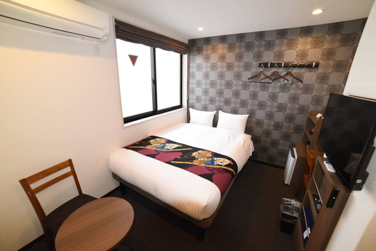 Una habitación de hotel con una cama, una silla, un televisor y una ventana.