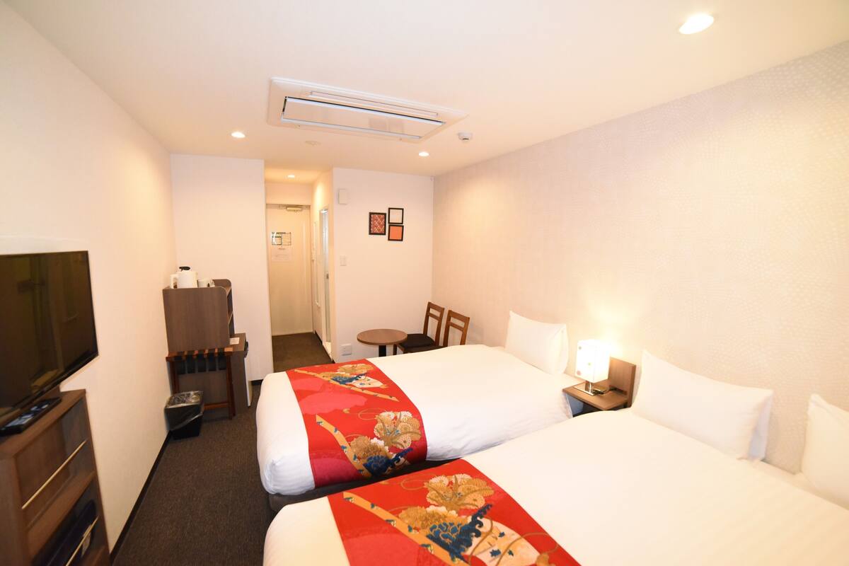 Habitación de hotel con dos camas, televisor, escritorio y una silla.