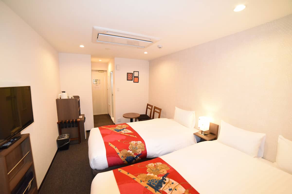 Quarto de hotel com duas camas, televisão, escrivaninha e uma cadeira.