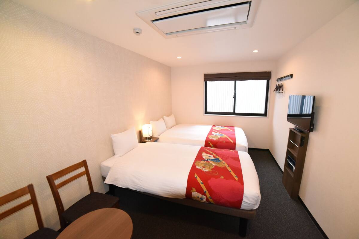Una habitación de hotel con dos camas, televisión, escritorio y silla.