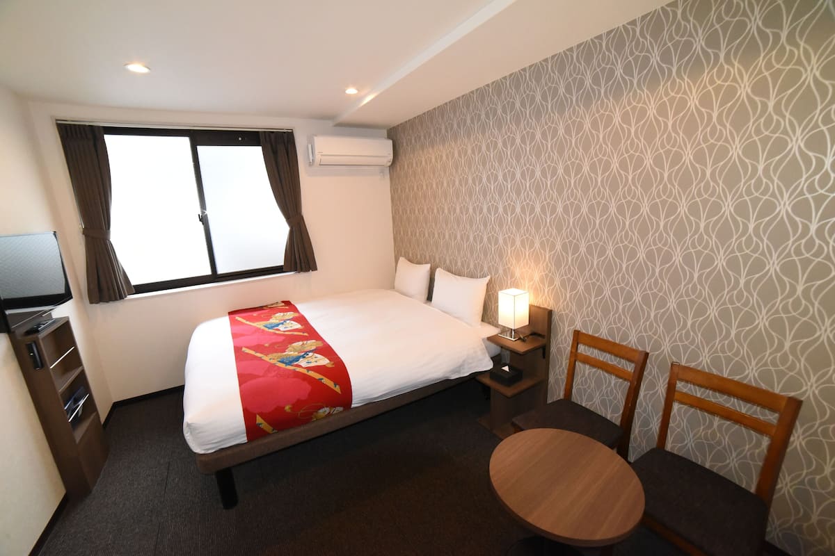 Habitación de hotel con cama, escritorio, silla, mesa y aire acondicionado.