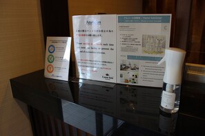 Un mostrador de recepción con carteles informativos sobre la higienización de manos y una botella de desinfectante.