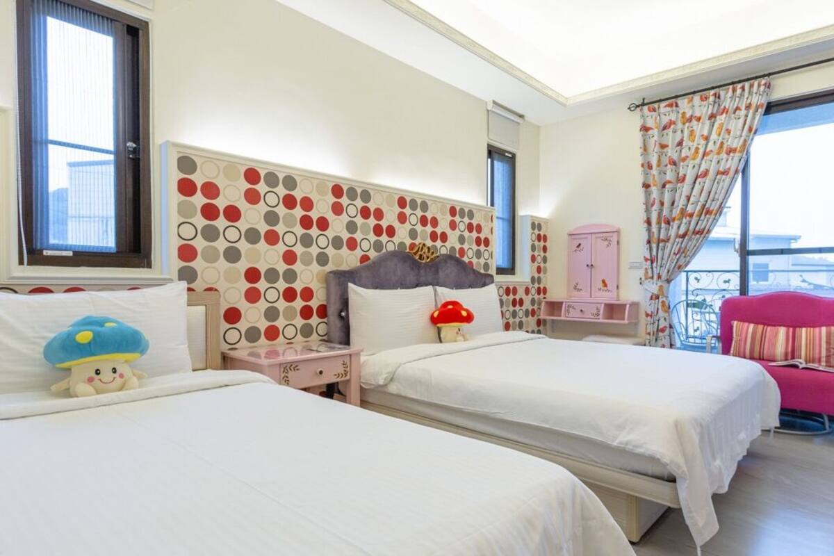 A hotel room with two beds, a large window with a view, a polka dot headboard, and a pink chair.