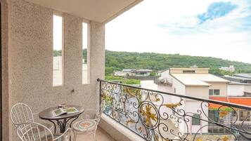A balcony with a table and chairs, a decorative railing, and a view of buildings and greenery.