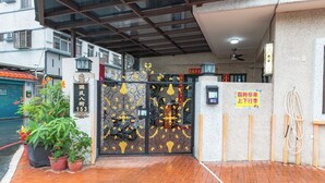 L’entrée d’un hôtel, agrémentée d’une grille décorative, de plantes en pot et d’un panneau indiquant la disponibilité de places de stationnement.