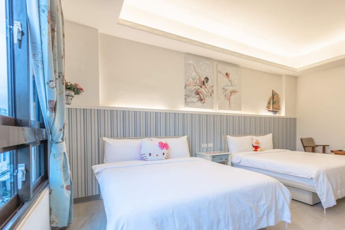 A hotel room with two beds, a window with curtains, a small table, and a chair.