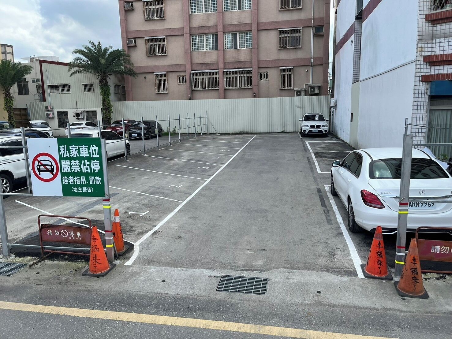 A parking lot with several cars, a sign indicating private parking, and a multi-story building in the background.