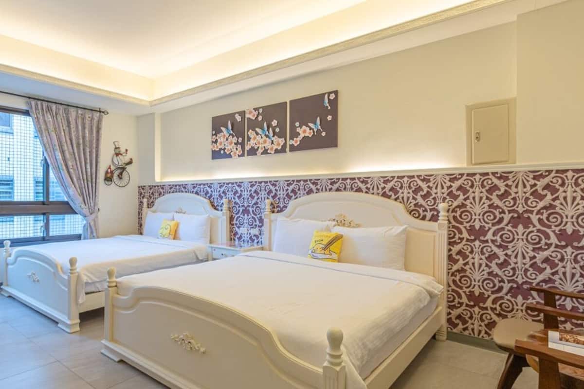 A hotel room with two beds, a window with curtains, and a wall with floral and bird artwork.
