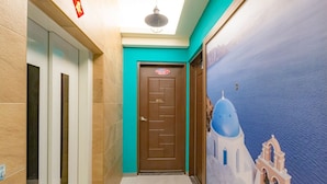 Un couloir avec un mur de couleur turquoise, une porte marron portant un numéro, et une fresque représentant un bâtiment à coupole bleue.