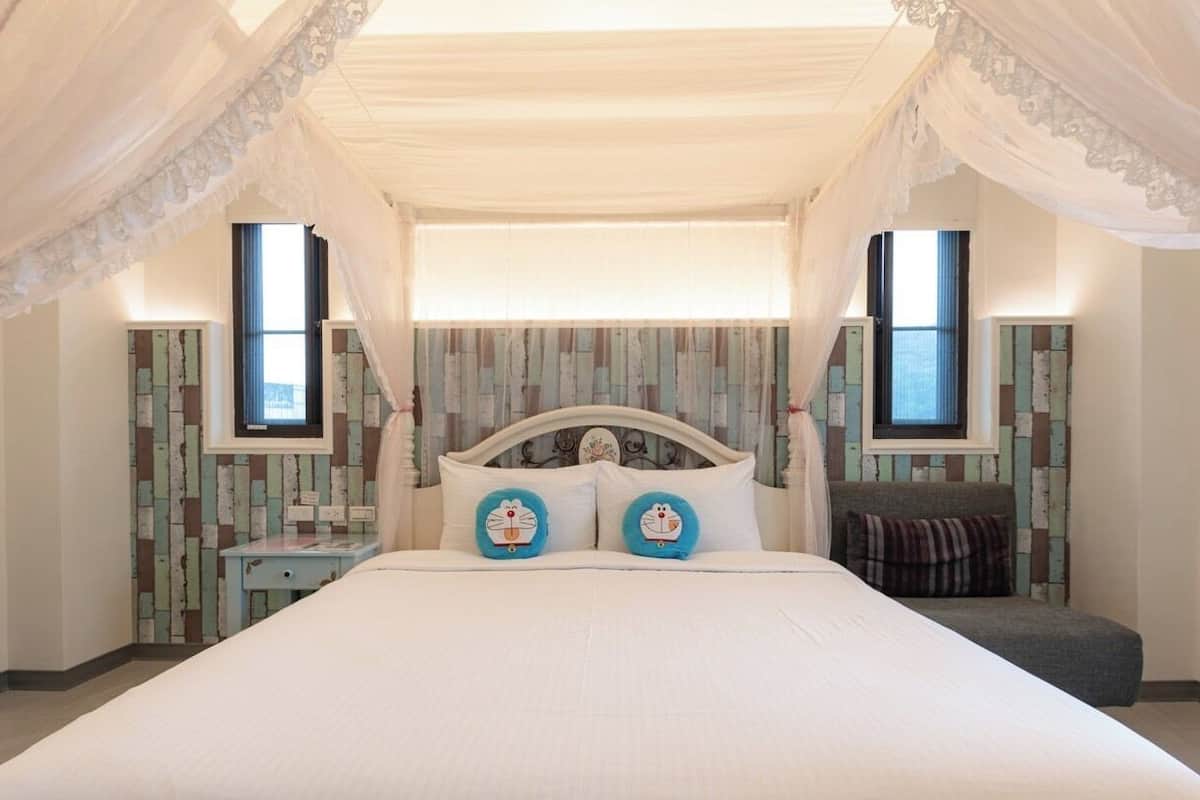 A bedroom with a large bed, a nightstand, a chair, and a window with curtains.