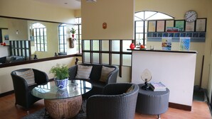 Un vestíbulo con muebles de mimbre, una mesa de vidrio y un reloj en la pared.