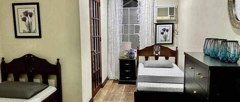 A bedroom with two beds, a dresser, a mirror, and a window with curtains.
