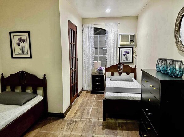A bedroom with two beds, a dresser, a mirror, and a window with curtains. - Cielo Vista BED and BREAKFAST (Tacloban)
