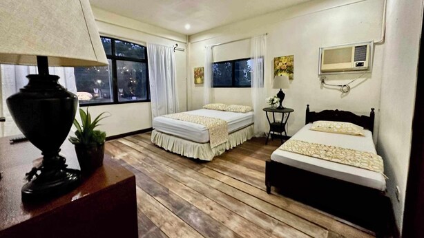 Habitación de hotel con dos camas, un ventanal grande, una lámpara de techo y una mesita con lámpara.