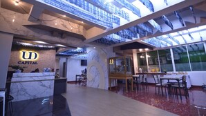 Un moderno vestíbulo de hotel con mostrador de recepción, suelo de mármol e iluminación azul con diseños en el techo.