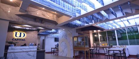 Un moderno vestíbulo de hotel con mostrador de recepción, suelo de mármol e iluminación azul con diseños en el techo.