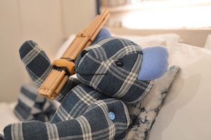Um brinquedo macio com tecido xadrez e detalhes em madeira, colocado sobre uma cama com roupa de cama estampada.