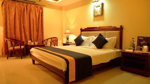 A hotel room with a large bed, wooden headboard, two bedside tables, a chair, a lamp, and a framed picture on the wall. - Hotel Grandeur (Hyderabad)