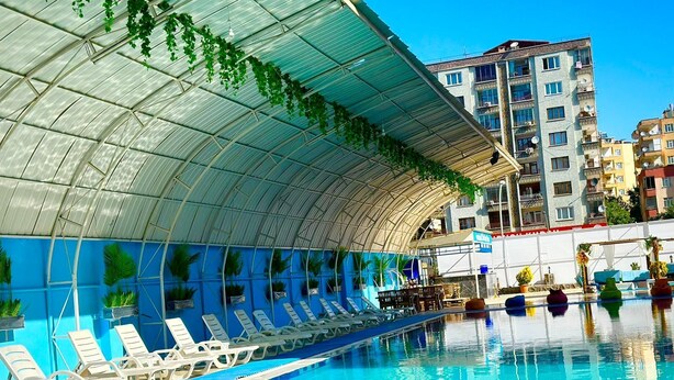 A swimming pool with white lounge chairs and a covered area with plants. - Malabadi Hotel (Diyarbakir)