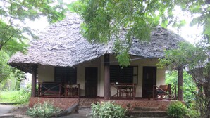 Een rieten hut met een veranda, houten meubels en een stenen fundering.