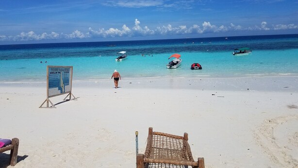 Een strand met helder turquoise water, een bord en een houten stoel.