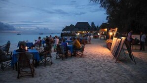 Een restaurant aan het strand met tafels en stoelen, met uitzicht op zee.