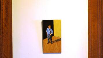 Una pintura muestra a una persona de pie en una habitación con suelo de madera y pared amarilla.