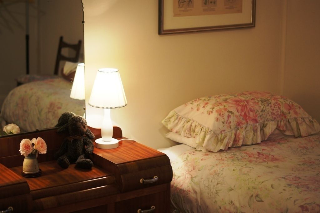 A bedroom with a wooden dresser, a lamp, a floral bedspread, and a teddy bear.