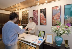 A reception desk with a white counter, a blue vase with flowers, and framed artwork on the wall. - Nishijin No Sato (Kyoto)