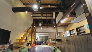 Un vaste espace de vie doté d’un plafond haut, de poutres en bois, d’une table à manger avec des coussins verts, d’un vélo et d’un téléviseur.