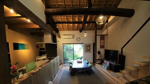 Une pièce spacieuse avec un plafond en bois, une table à manger avec des chaises, un téléviseur et un escalier.