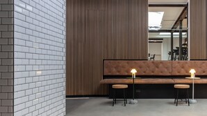 Un interior moderno con pared de ladrillo, revestimiento de madera, un banco acolchado marrón y dos taburetes con una lámpara de mesa.
