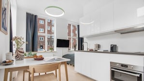 Una cocina moderna con armarios blancos, horno empotrado y comedor con mesa y sillas de madera.