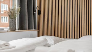 Habitación de hotel con pared de listones de madera, una mesita de noche con una planta y camas impecablemente preparadas.